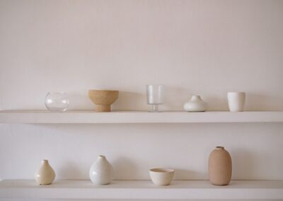 Elegant arrangement of ceramic and glass vessels on minimalist shelves within a neutral indoor setting.