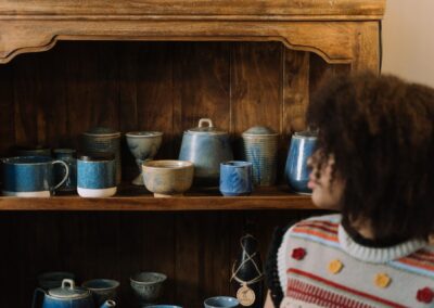 A cozy scene of blue ceramic pottery on a wooden shelf with a person admiring the collection.